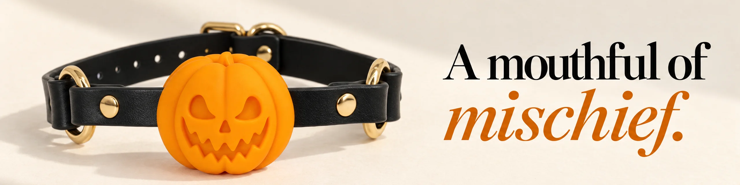 A mouthful of mischief. Orange Pumpkin Gag with black straps and yellow-gold hardware on a cream backdrop.